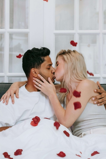 couple kissing in bed with rose petals