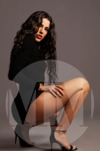 London escort Amal squatting down wearing a black dress