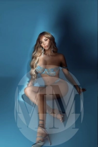 Carmen leaning back in light blue lingerie and strappy stilettos.