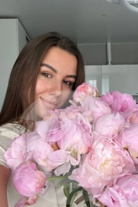 Crystal taking a selfie holding pink flowers and smiling.