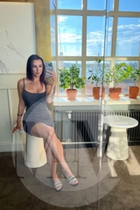 Crystal taking a selfie in a restaurant wearing a short and tight grey dress