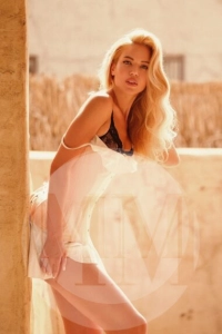 Dubai escort Elena leaning against a wall wearing a white dress