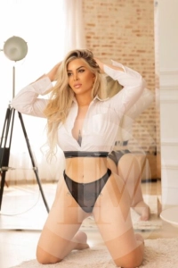 London escort Zaya kneeling on the floor with her hands on her head